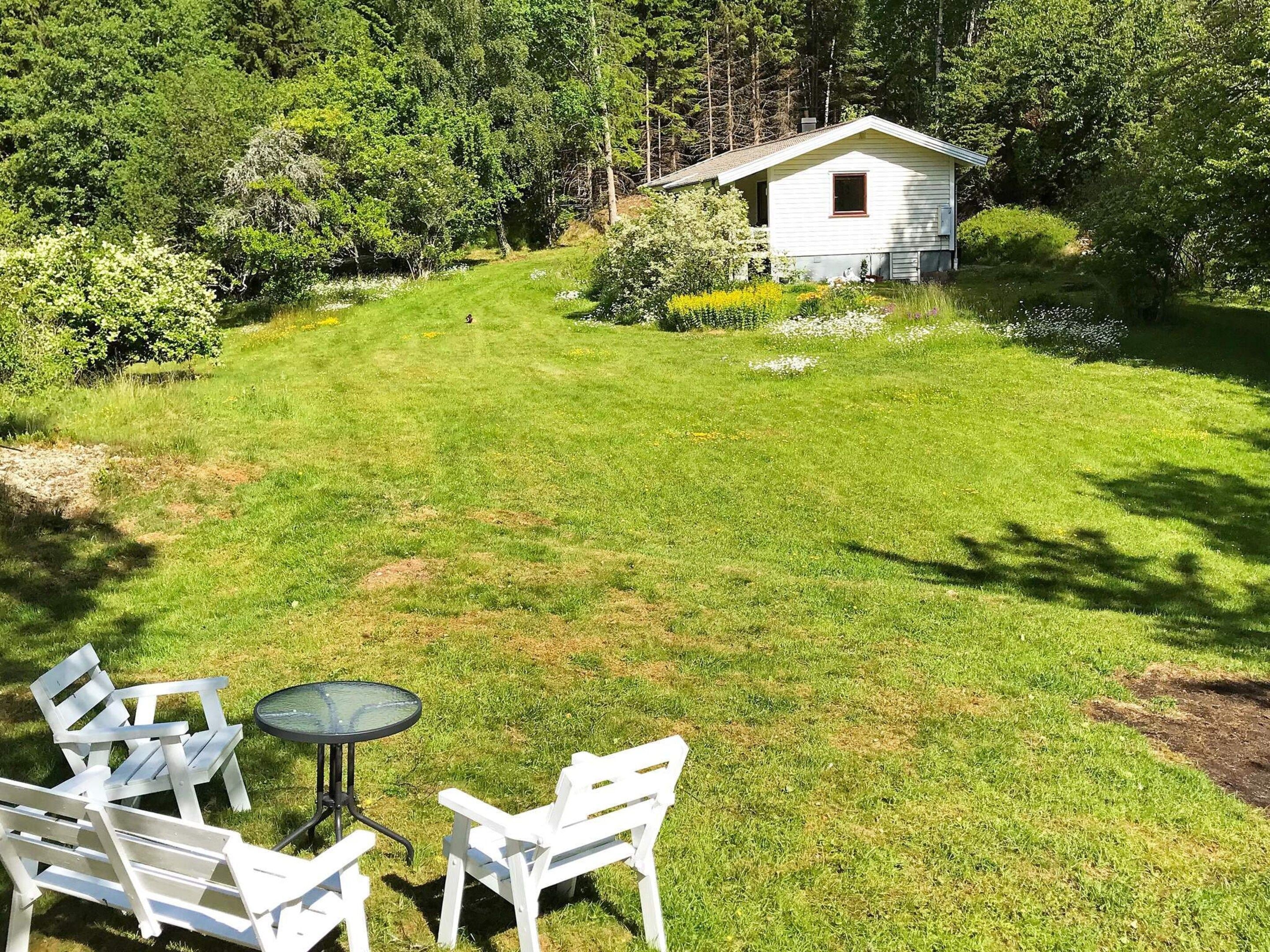 A grassy yard with a small white house, a table, and two chairs.
