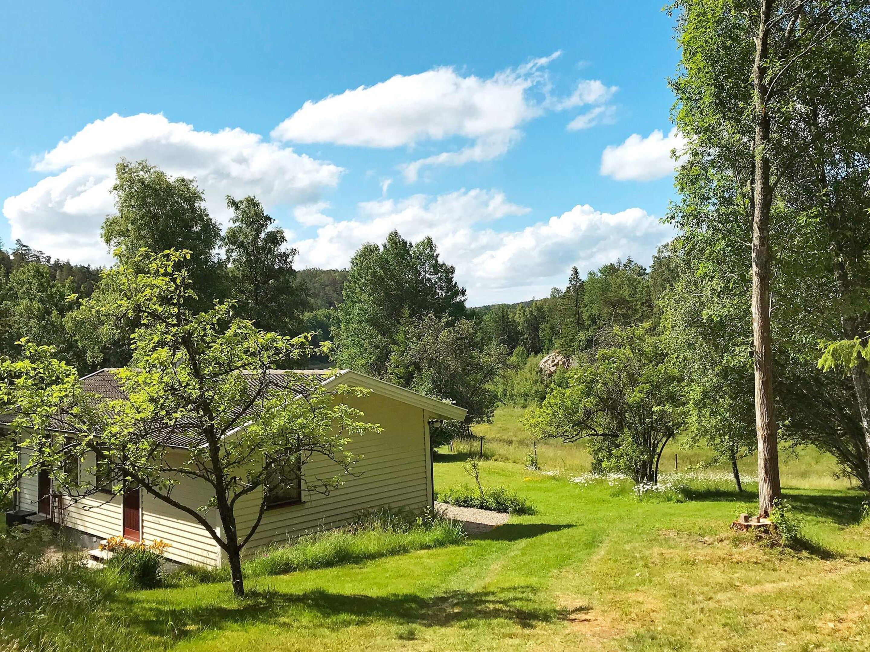A single-story house with a sloped roof, surrounded by a grassy yard and trees.
