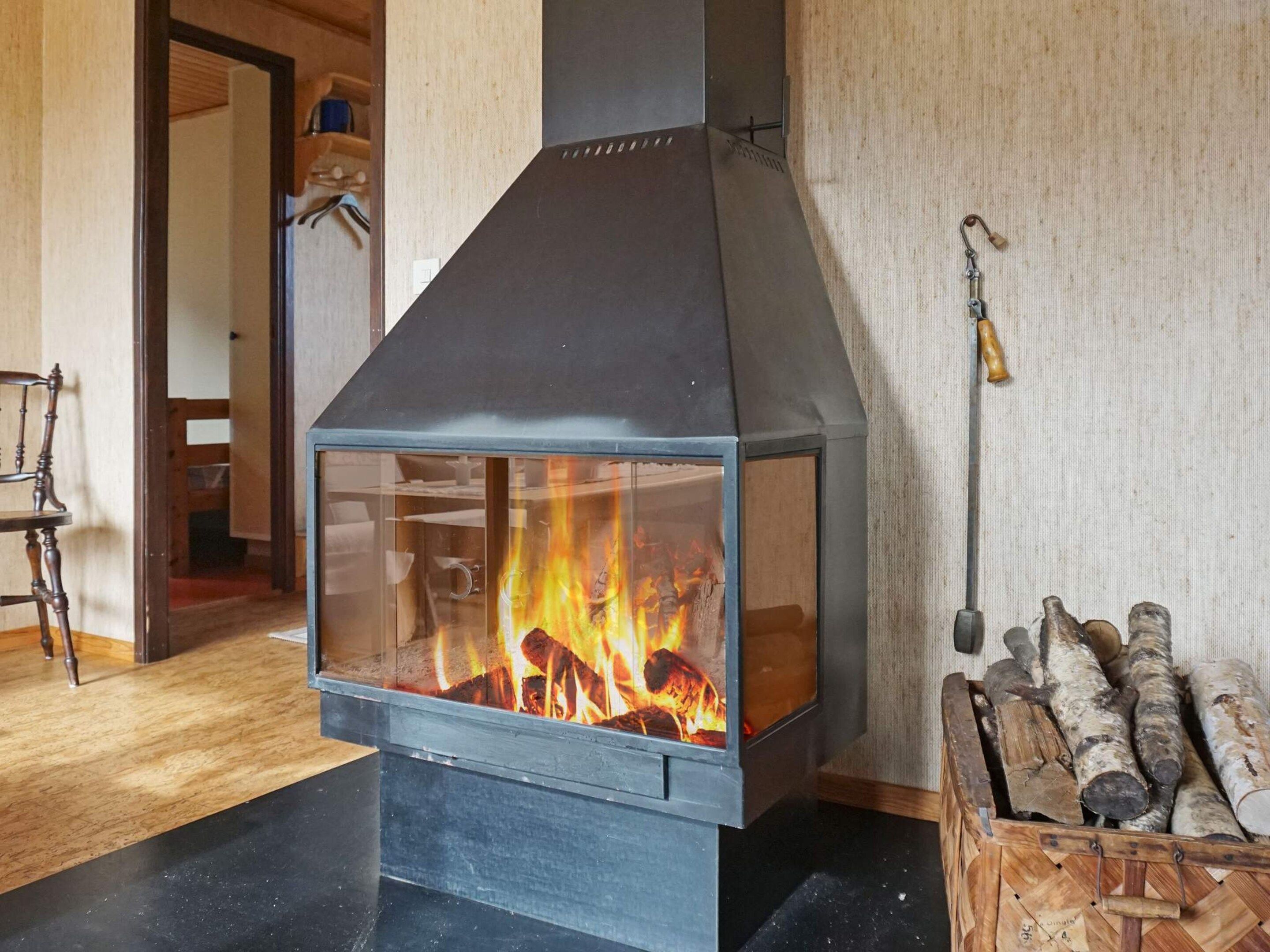 A modern fireplace with a glass front, logs inside, and a chimney.