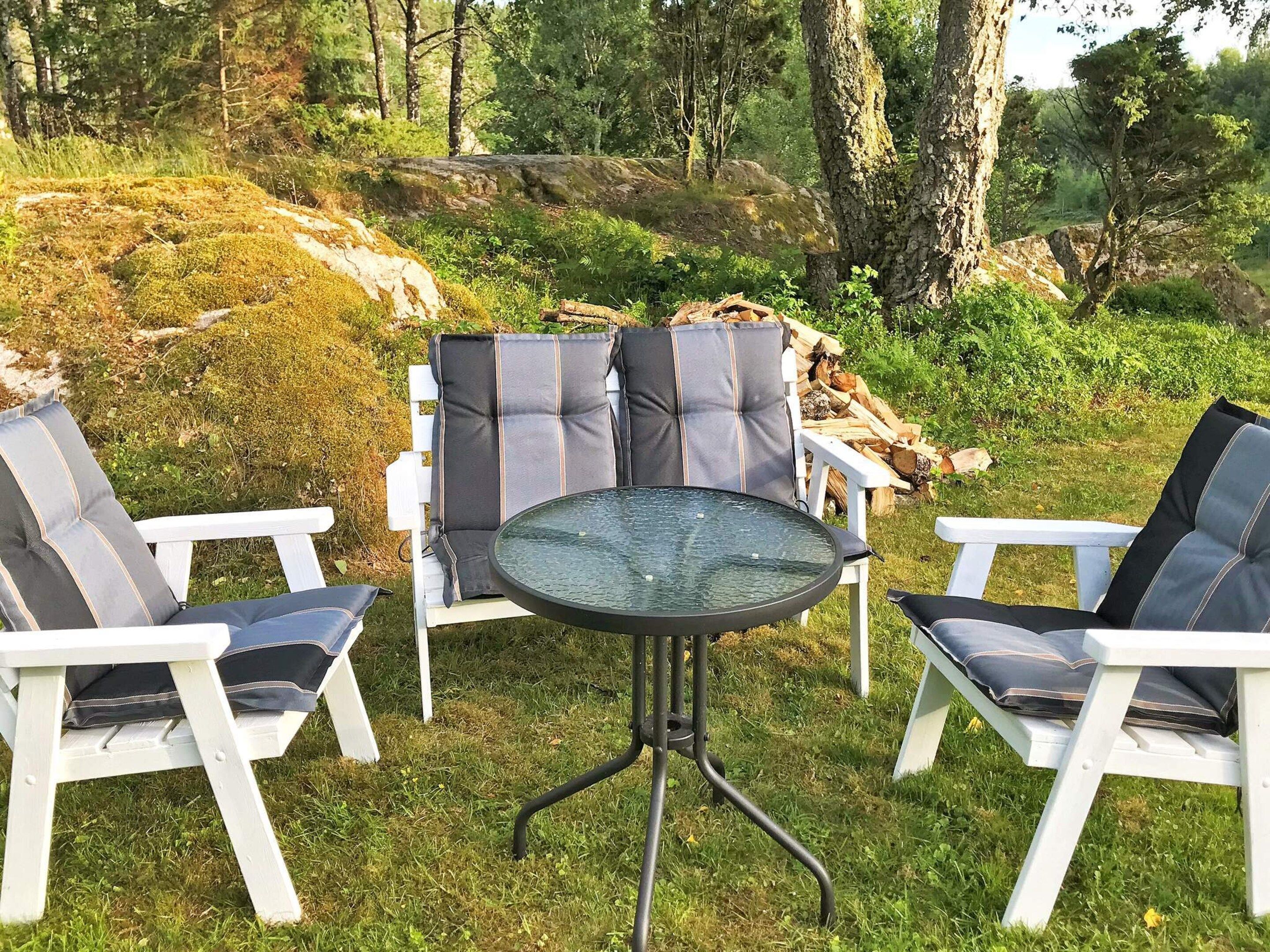 Un área de estar al aire libre con sillas blancas y una mesa de vidrio, rodeada de follaje y árboles.