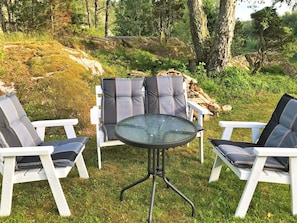 An outdoor seating area with white chairs and a glass table, surrounded by greenery and trees. - 4 Person Holiday Home in Dingle (Dingle)