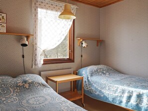 Una habitación con dos camas individuales, una mesita de madera, un ventanal con cortina y lámparas fijadas a la pared.