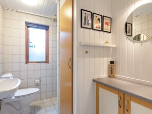 A bathroom with a toilet, sink, and a shelf with a mirror and framed pictures. - 4 Person Holiday Home in Hals-by Traum (Hals)