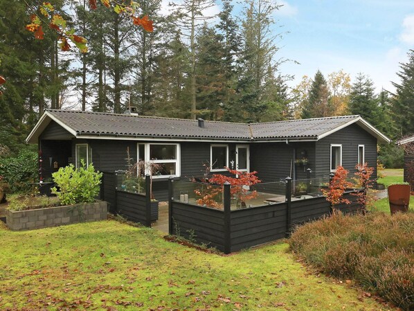 A small, dark-colored wooden house with a fenced deck, surrounded by a garden and trees. - 4 Person Holiday Home in Hals-by Traum (Hals)