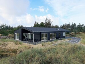 A modern house with a dark exterior, large windows, and a covered outdoor seating area. - 5 Star Holiday Home in Oksbol (Oksbol)