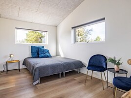 A modern bedroom with a bed, two windows, a chair, a small table, and a plant.
