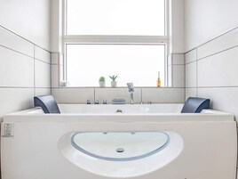 Un baño con una bañera grande, un lavabo con recipiente de vidrio y una ventana sobre el lavabo.