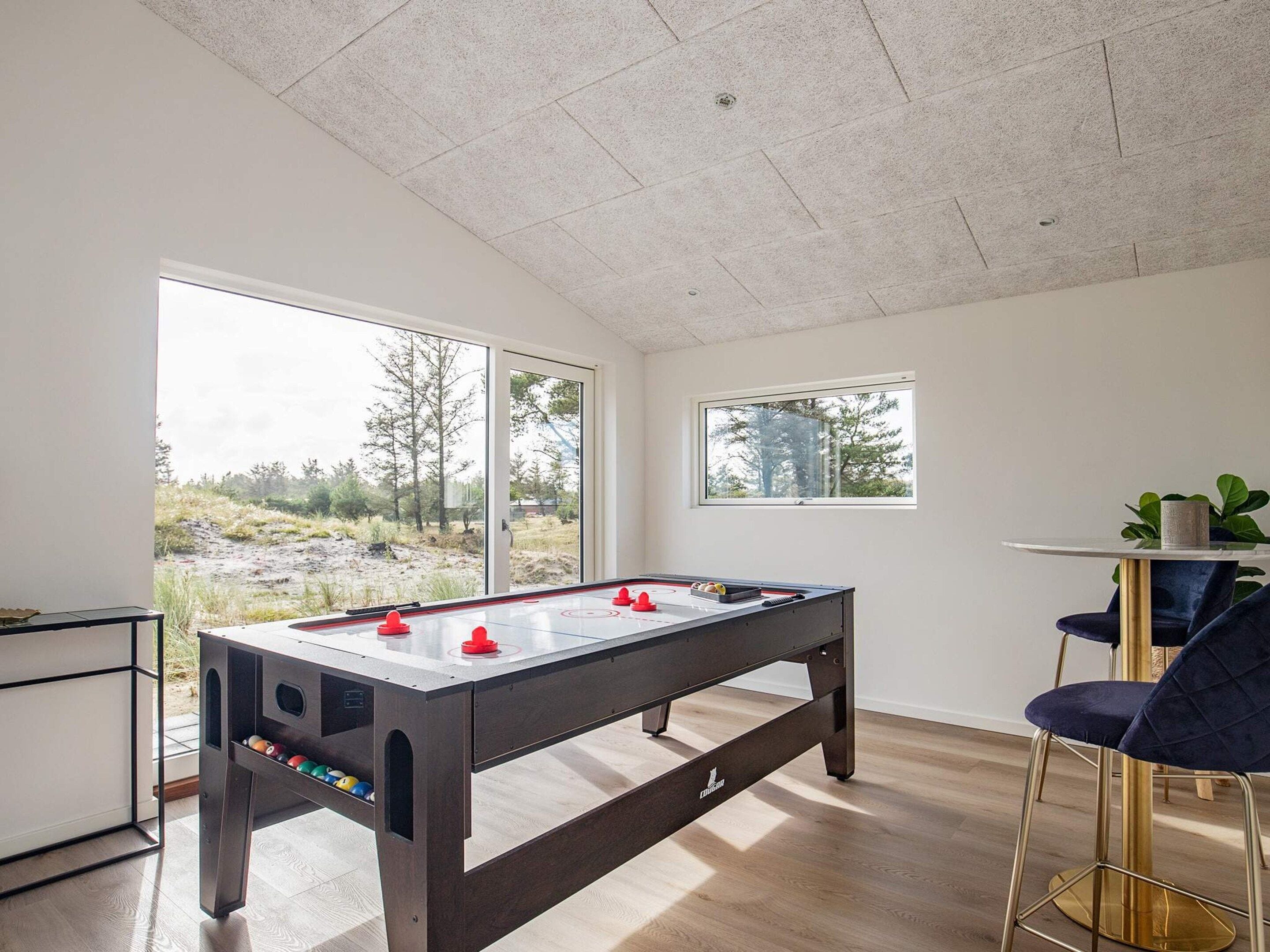 Una habitación moderna con mesa de futbolín, barra y amplias ventanas que ofrecen vistas al exterior.