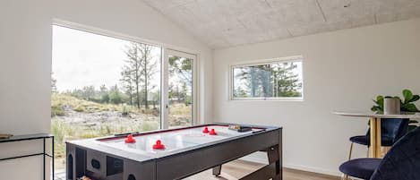 A modern room with a foosball table, a bar area, and large windows offering a view of the outdoors.