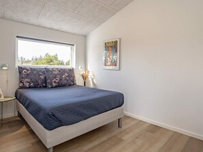 Et soveværelse med en seng, et vindue, et billedværk på væggen og et lille sengebord.