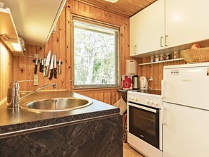 A compact kitchen with a sink, stove, and window overlooking a forest. - 5 Person Holiday Home in Stege (Stege)