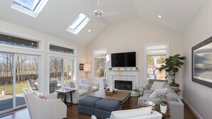 A spacious living room with a fireplace, comfortable seating, and large windows. - Southampton Family Summer (Southampton)