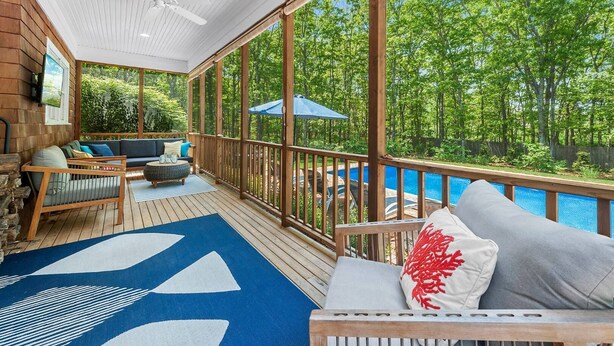 A covered deck with a pool, wooden furniture, and a view of the surrounding greenery. - Southampton Family Summer (Southampton)