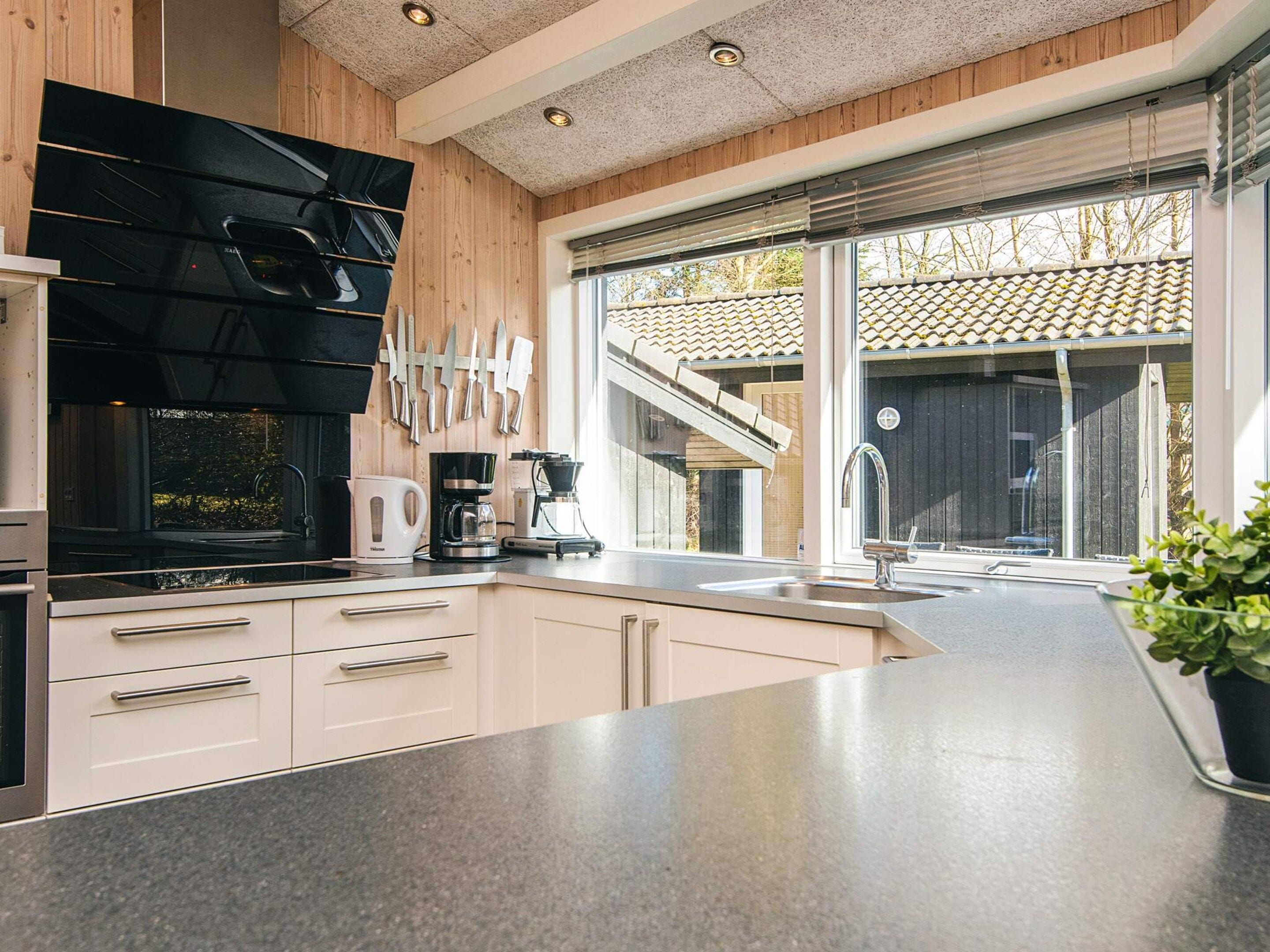 A modern kitchen with a built-in stove, a coffee maker, and a large window with a view of a house.