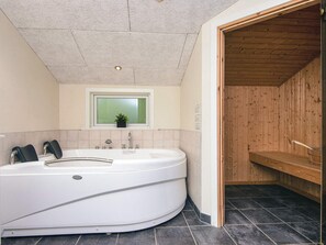 Een moderne badkamer met een vrijstaand bad, een raam met plant en een houten sauna.