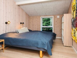 Un dormitorio con una cama, dos lámparas fijadas a la pared, una ventana con vista a zonas verdes y suelo de madera.