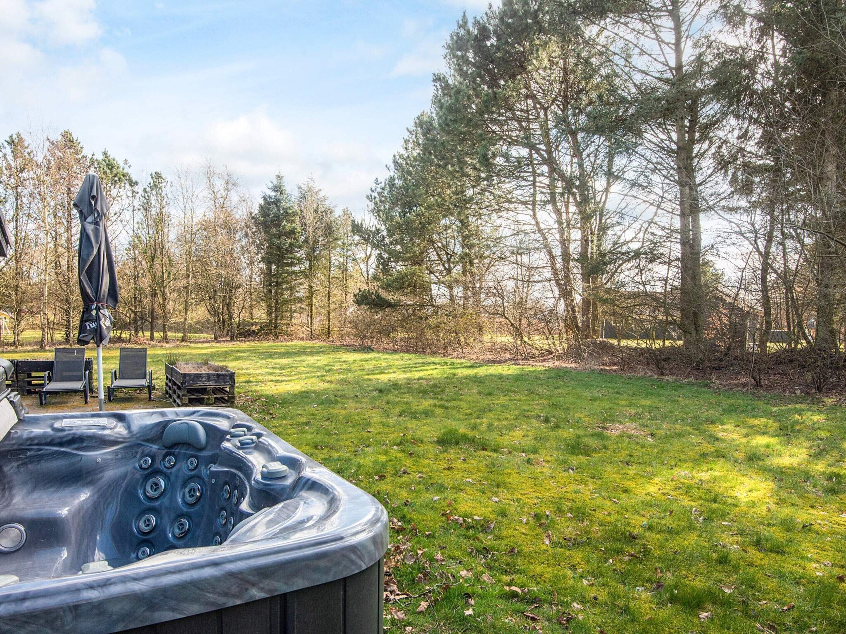 A hot tub in a grassy outdoor area with lounge chairs and a covered umbrella.