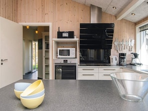 A modern kitchen with wooden paneling, a microwave, oven, and a coffee maker. - 4 Star Holiday Home in Oksbol (Oksbol)