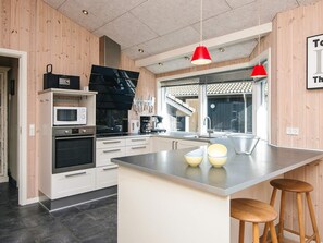 Una cocina moderna con una isla central, electrodomésticos de acero inoxidable, armarios de madera y lámparas colgantes rojas.