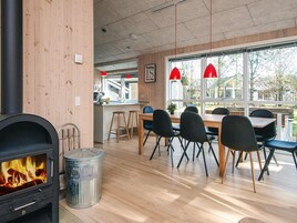 Una cocina moderna con estufa de leña, zona de comedor con sillas y una mesa, y ventanas amplias con vistas al exterior.