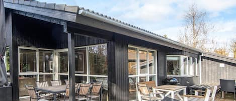 A covered patio with outdoor furniture, large windows, and a wooden deck.