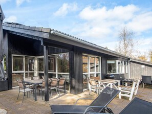 Een overdekt terras met buitenmeubilair, grote ramen en een houten terras.