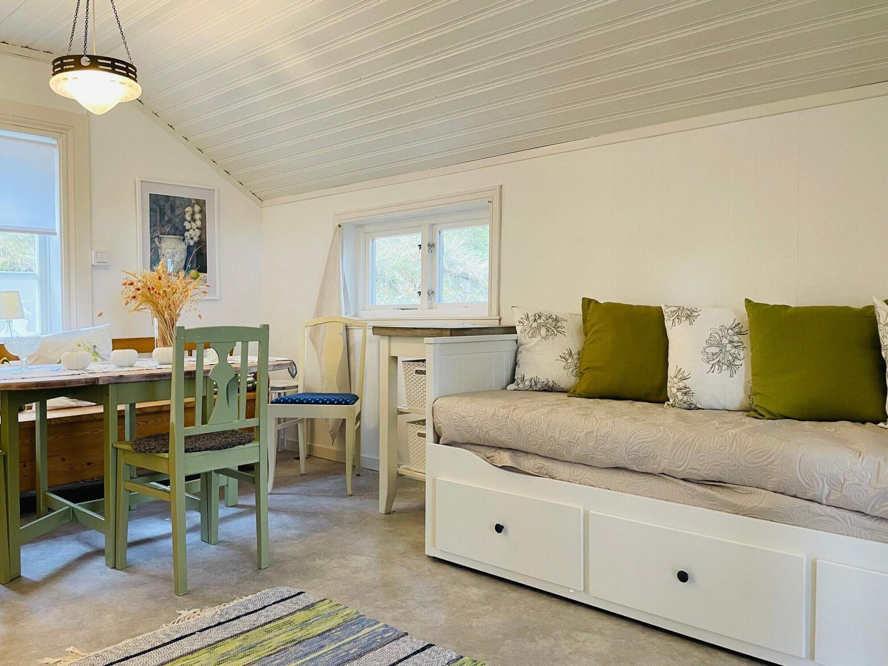 A cozy room with a dining table, chairs, a sofa with storage drawers, and a window with curtains.