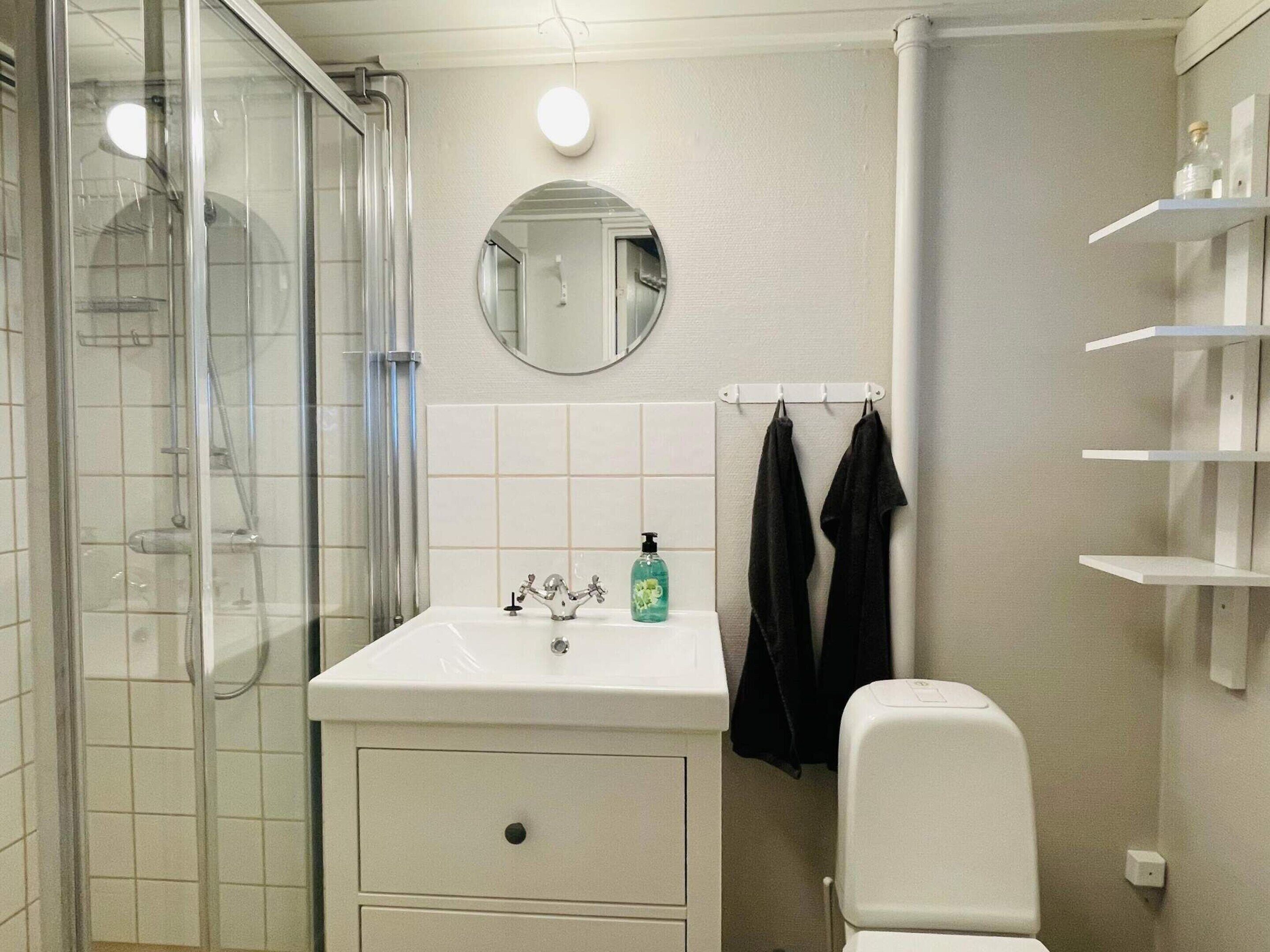 A bathroom with a glass shower enclosure, a white sink with a soap dispenser, a mirror, and a towel rack with two towels.