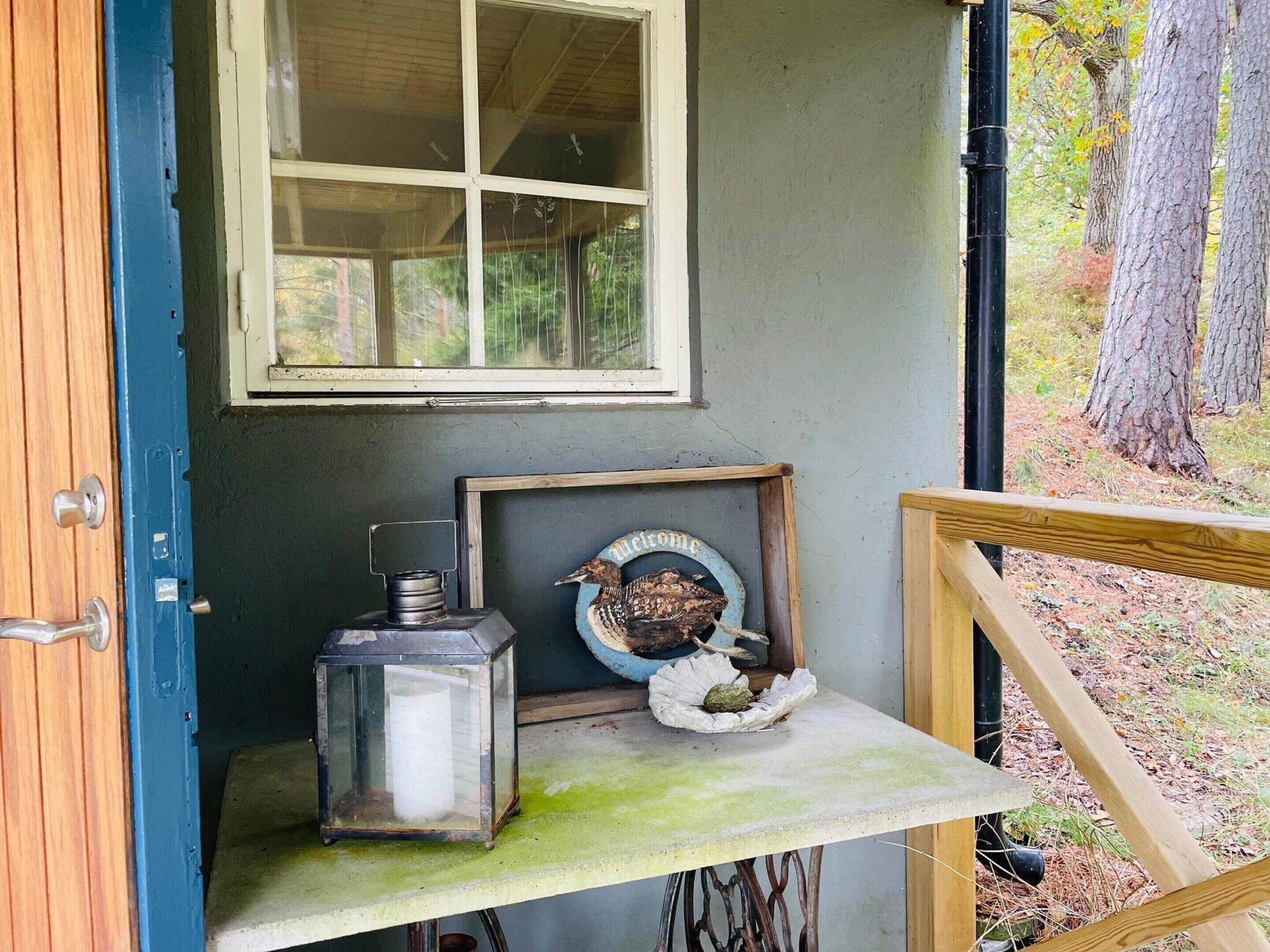En lille veranda med en trædør, et vindue, et bord med en lygte og et velkommenskilt.