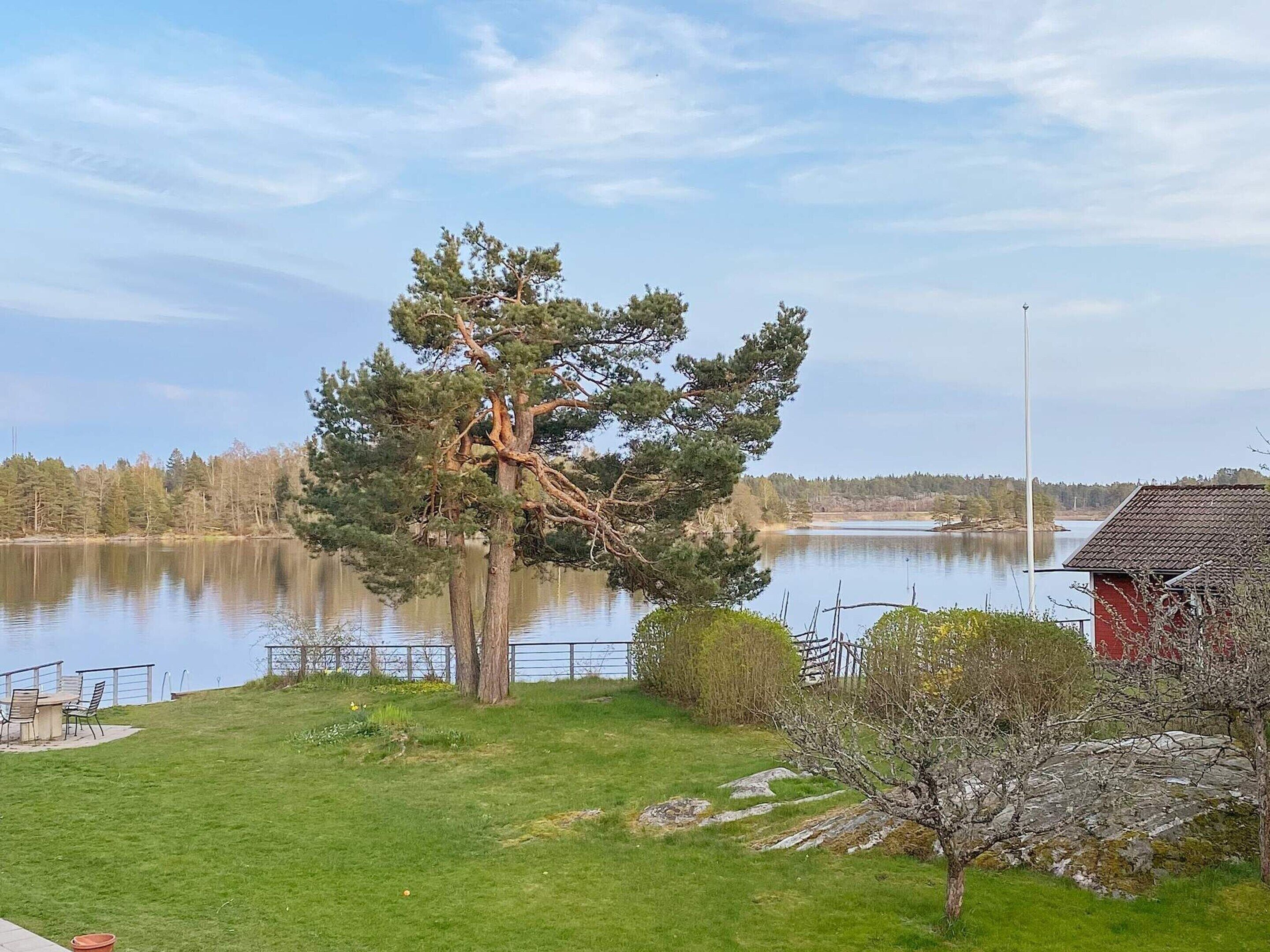 A lakeside property with a large tree, a red building, and a grassy area with outdoor furniture.