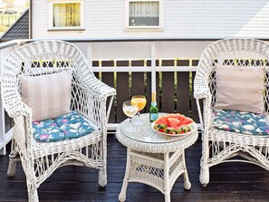 Two wicker chairs with floral cushions on a balcony. A small round table with a glass of wine, a bottle, and a plate of watermelon slices is between them. - 5 Person Holiday Home in Frederikstad (Fredrikstad)