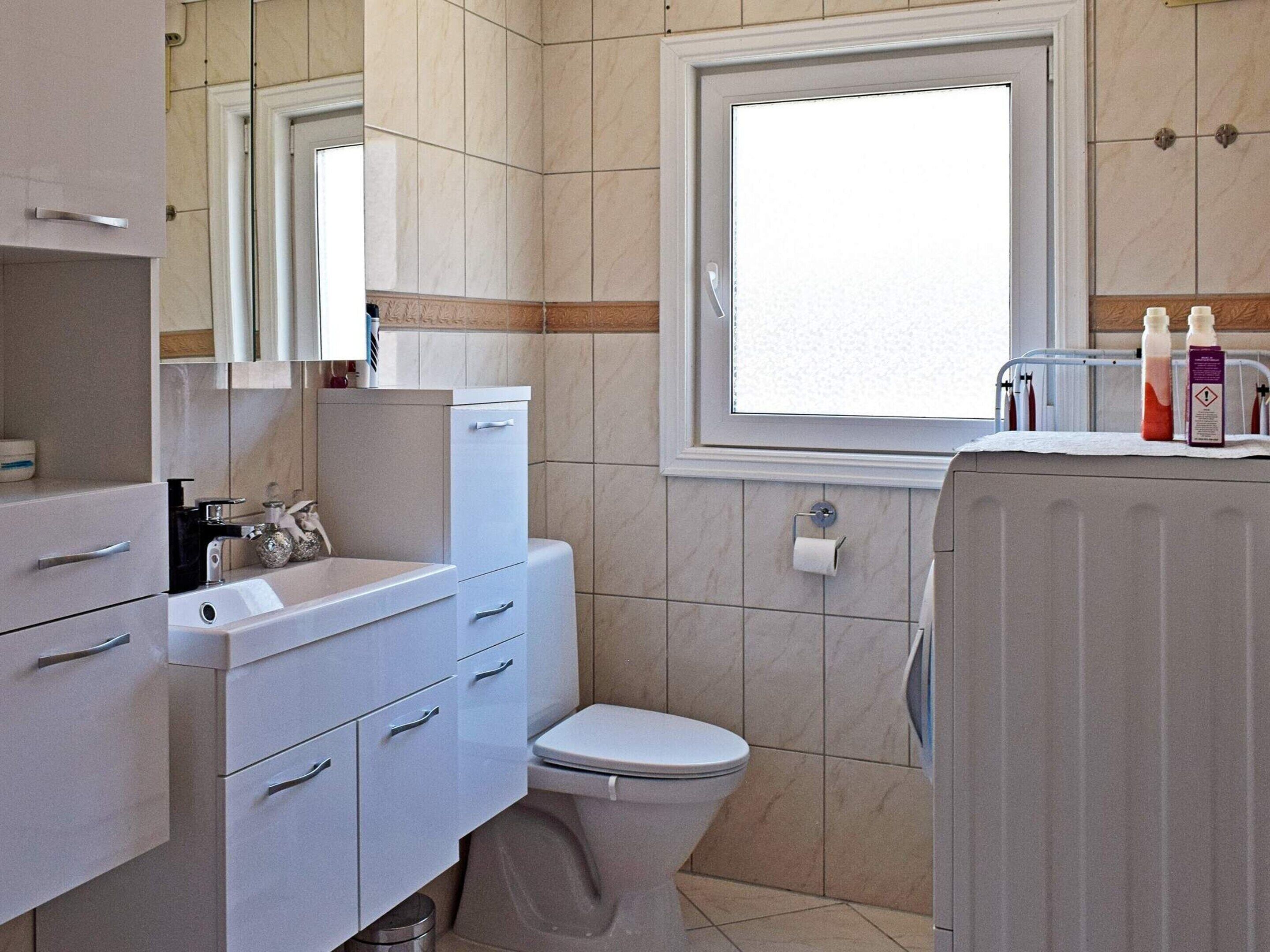 A bathroom with a toilet, sink, mirror, and window.