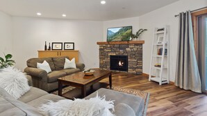 A living room with a stone fireplace, a sofa, a coffee table, and a bookshelf. - Ask about summer discounts! Walk to Govy/Ski Bowl, Garage parking, Sleeps 8 (Government Camp)