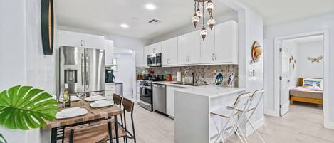 A modern kitchen with white cabinetry, stainless steel appliances, and a central island with seating.