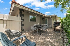 Une terrasse avec une table et des chaises, un barbecue et une clôture blanche.