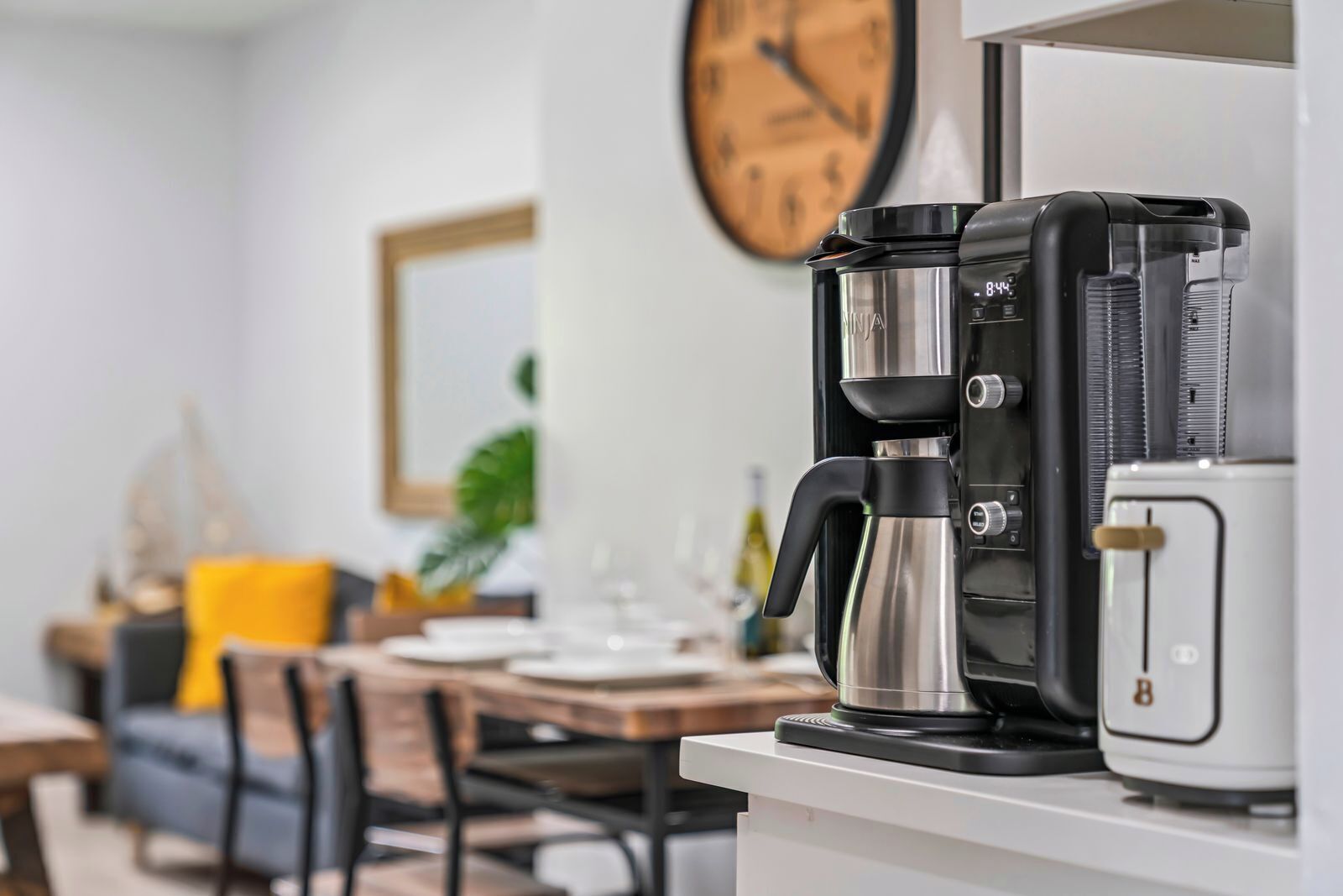 Une cuisine équipée d’une machine à café, d’un grille-pain et d’un coin repas comprenant une table, des chaises et une horloge murale.