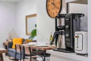A kitchen with a coffee maker, toaster, and a dining area with a table, chairs, and a clock on the wall. - Spotless 2BR Duplex, 5 Min to the Beach, Beach and Baby Gear Included (Pompano Beach)