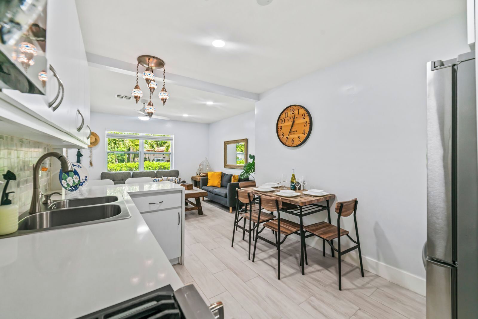 Une cuisine moderne avec un coin repas, une grande horloge murale et une vue sur la verdure à l’extérieur.