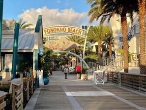 A boardwalk leading to a beach entrance with palm trees and a sign reading "Compano Beach". - Spotless 2BR Duplex, 5 Min to the Beach, Beach and Baby Gear Included (Pompano Beach)