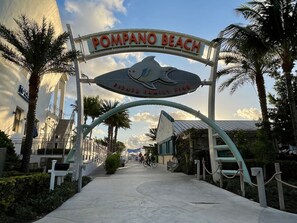 A sign for 'Pompano Beach Fisher Family Pier' with a pathway leading to a building. - Spotless 2BR Duplex, 5 Min to the Beach, Beach and Baby Gear Included (Pompano Beach)
