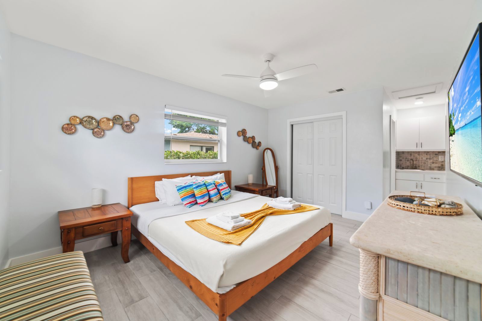 A hotel room with a bed, a bedside table, a mirror, a window, a ceiling fan, and a TV.