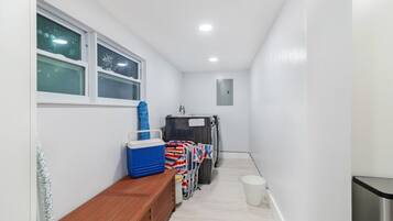 A narrow hallway with a bench, a window, a trash bin, and a laundry cart.