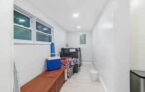 A narrow hallway with a bench, a window, a trash bin, and a laundry cart.