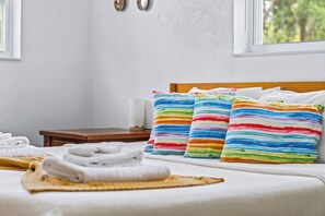 A neatly made bed with colorful striped pillows, a bedside table with a lamp, and a view of trees through the window.