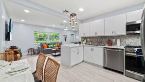 Una cocina moderna con armarios blancos, electrodomésticos de acero inoxidable y un comedor con mesa para cuatro.