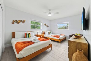 A hotel room with two beds, a ceiling fan, a TV, and a wooden nightstand with a basket.