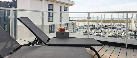 Un balcone con due poltrone e un tavolino con frutta, con vista su una marina piena di barche.