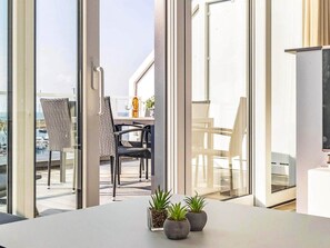 Un interior moderno con ventanas amplias, un comedor con sillas y plantas en macetas sobre una mesa.