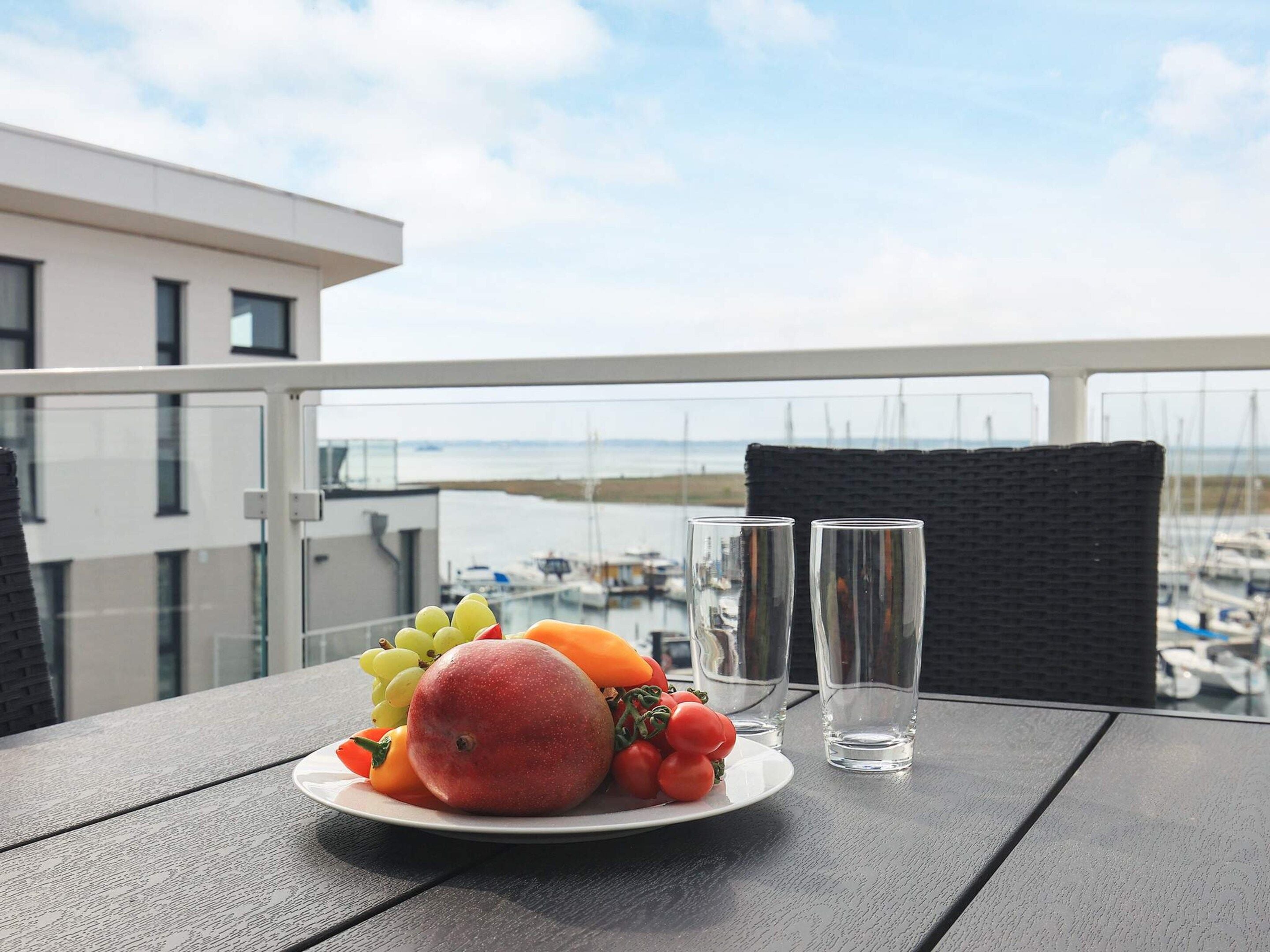 Ein Balkon mit einem Esstisch, der mit Geschirr und Obst sowie zwei Gläsern gedeckt ist.