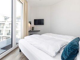 Habitación de hotel con cama, televisor de pantalla plana montado en la pared, una mesita con un jarrón de flores y un ventanal con vistas al exterior.